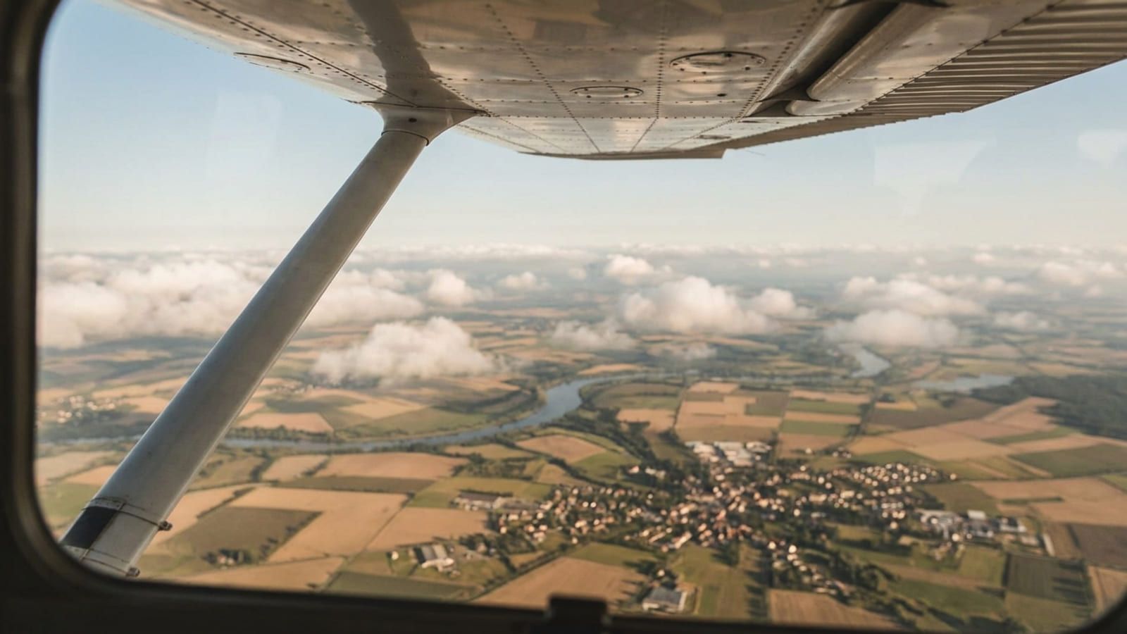 Blick aus dem Seitenfenster eines Hochdeckers auf Felder und einen Fluss