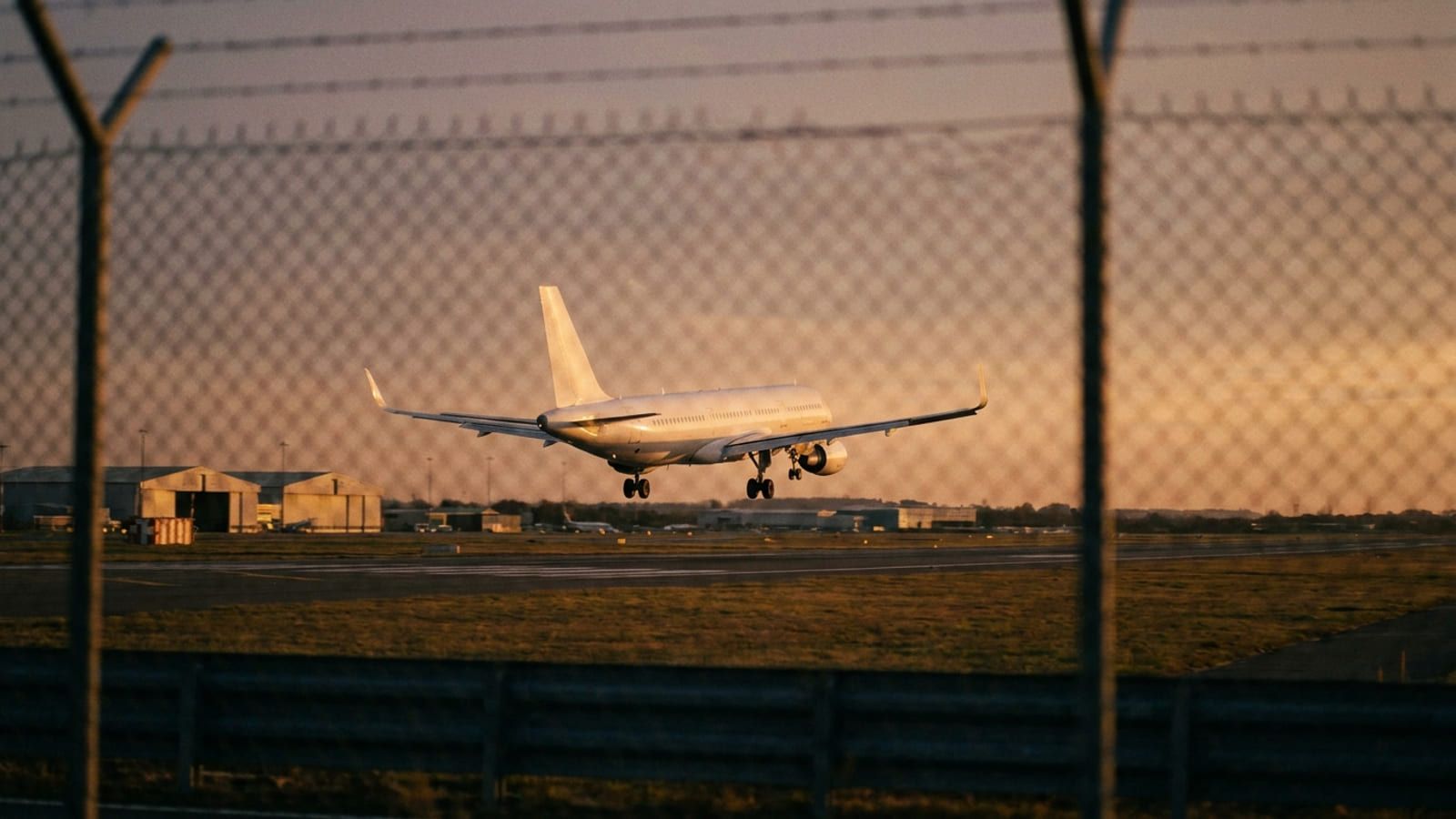 Flughafenzaun im Vordergrund, dahinter ein Flugzeug im Endanflug